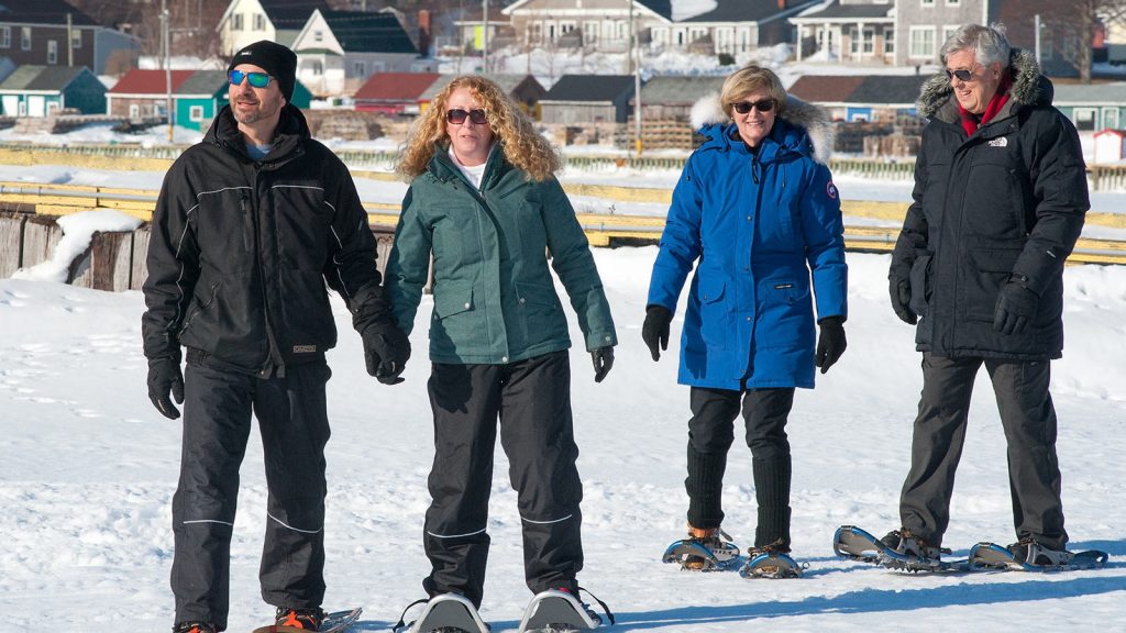 A group of people snowshoeing on a sunny winter day in Prince Edward Island, with colorful houses in the background.