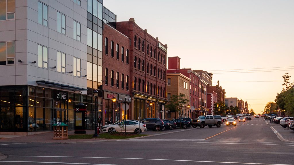 A street view of downtown Charlottetown, Prince Edward Island, at sunset with cars parked along the road and storefronts lining the street.